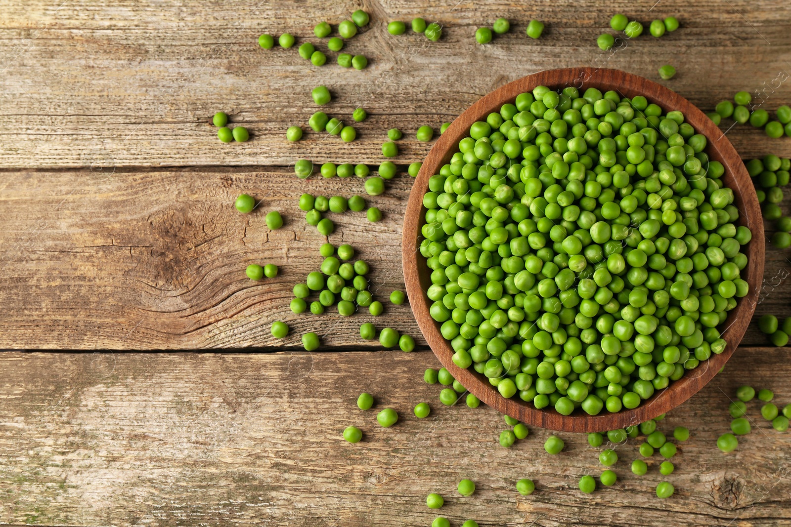 Photo of Fresh green peas in bowl on wooden table, top view. Space for text