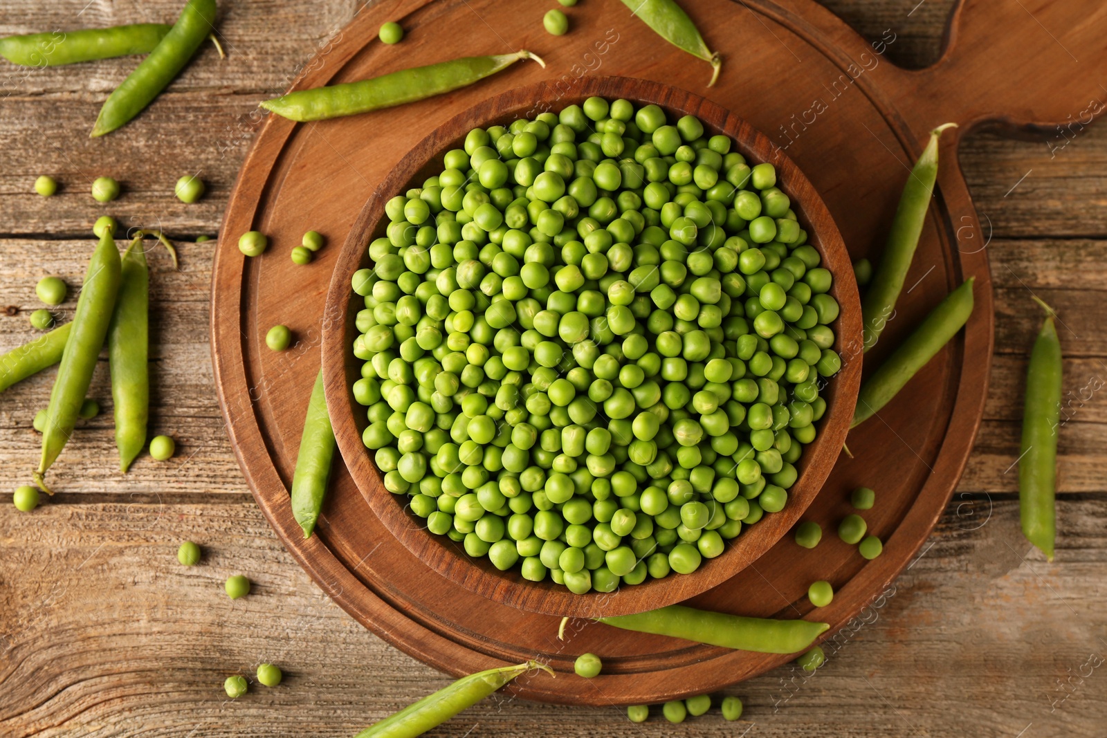 Photo of Fresh green peas in bowl and pods on wooden table, flat lay