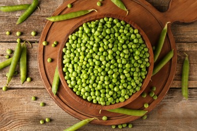 Fresh green peas in bowl and pods on wooden table, flat lay