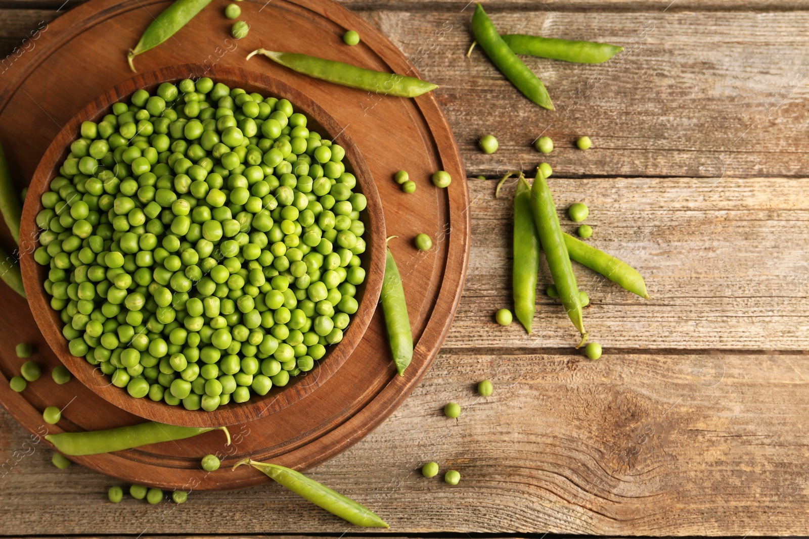 Photo of Fresh green peas in bowl and pods on wooden table, flat lay. Space for text