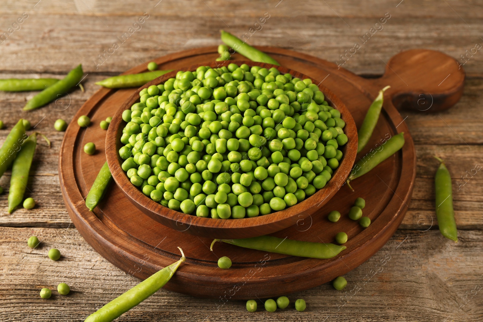 Photo of Fresh green peas in bowl and pods on wooden table