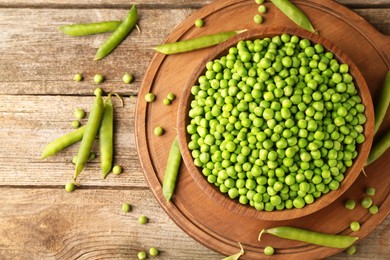 Photo of Fresh green peas in bowl and pods on wooden table, flat lay