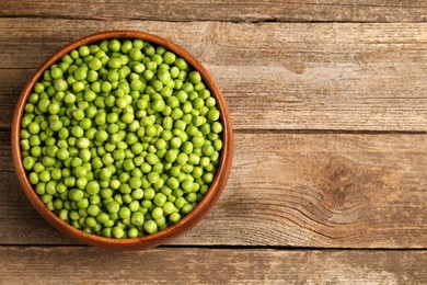 Photo of Fresh green peas in bowl on wooden table, top view. Space for text