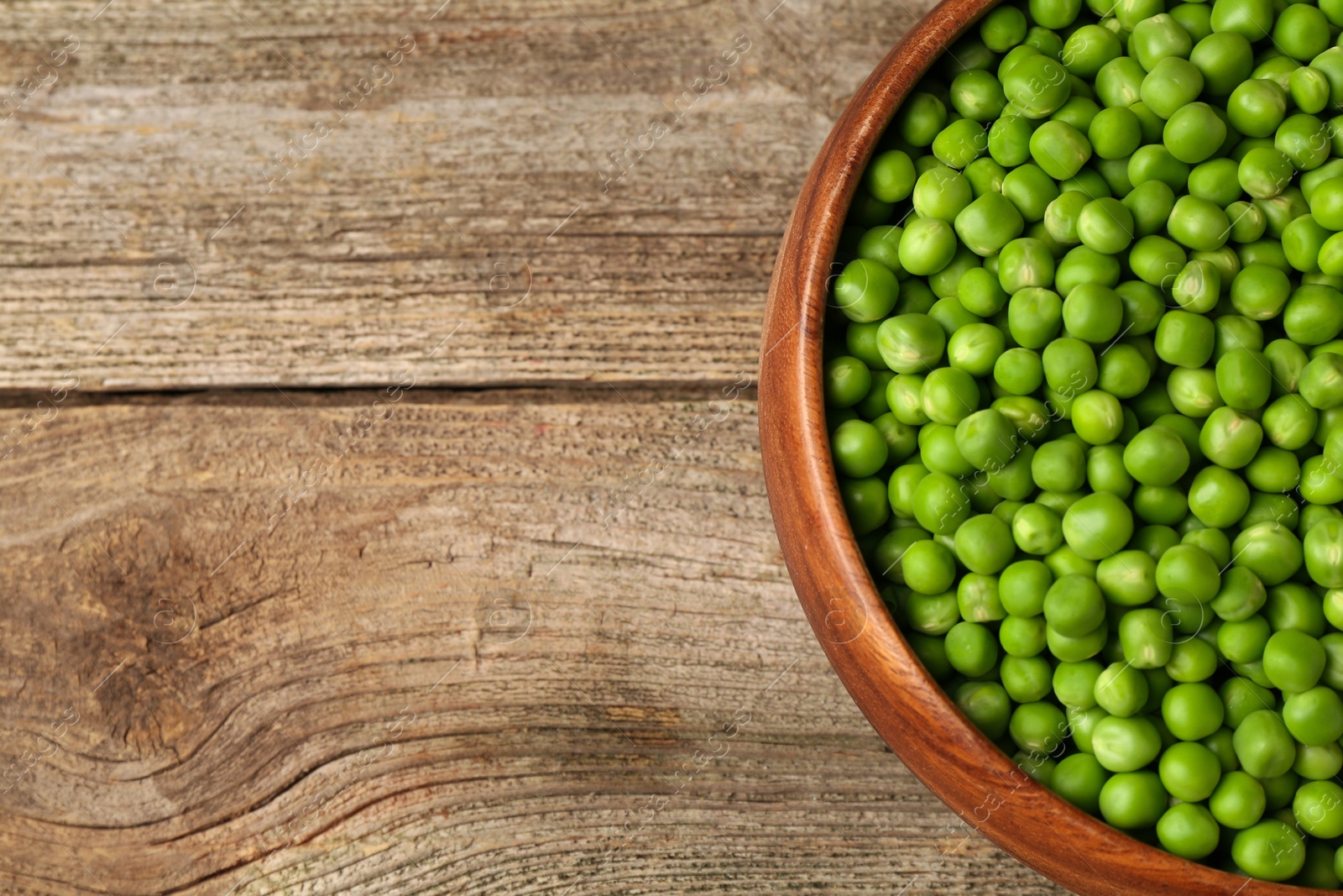 Photo of Fresh green peas in bowl on wooden table, top view. Space for text