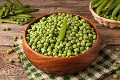 Photo of Fresh green peas and pods in bowl on wooden table, closeup