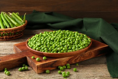 Fresh green peas in bowl and pods on wooden table