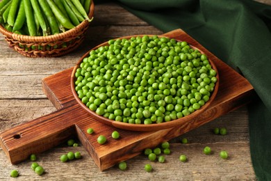 Photo of Fresh green peas in bowl and pods on wooden table