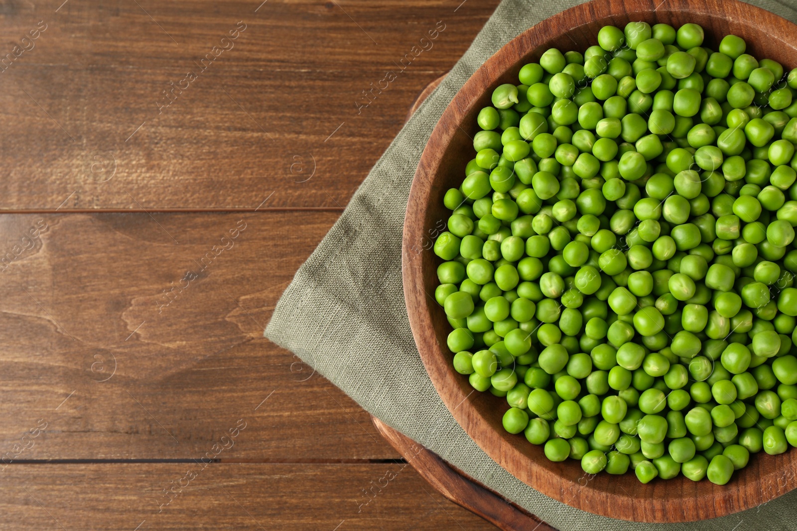 Photo of Fresh green peas in bowl on wooden table, top view. Space for text