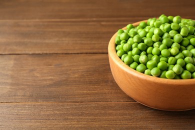 Fresh green peas in bowl on wooden table, space for text