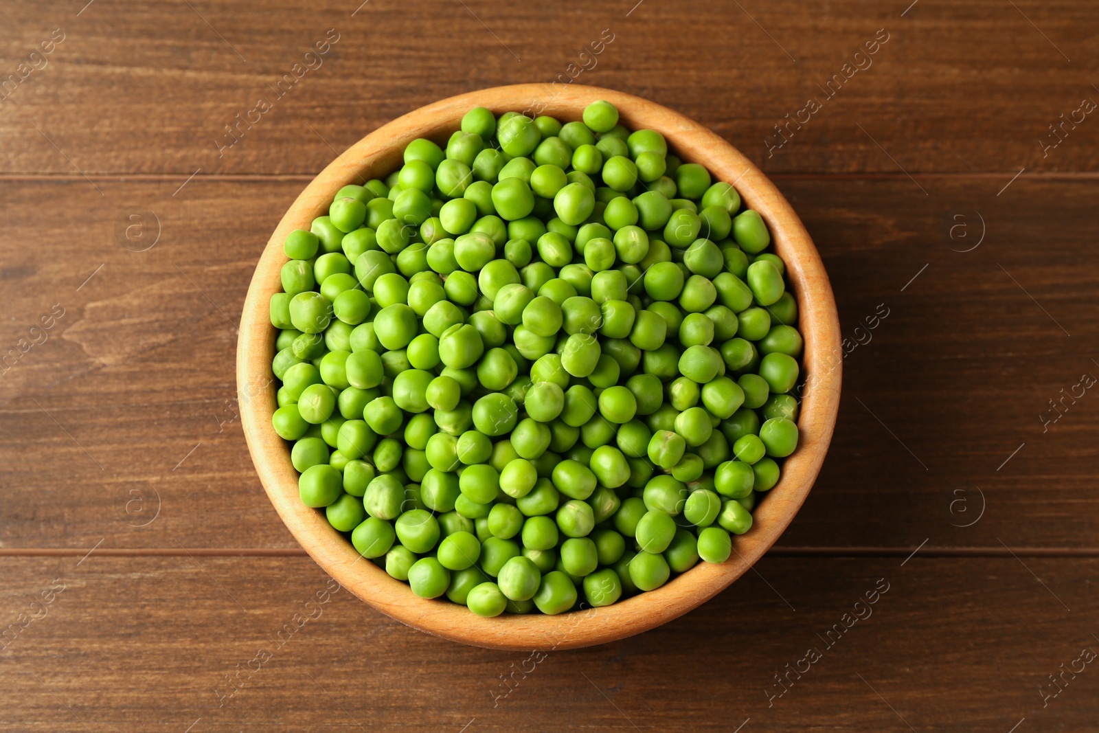 Photo of Fresh green peas in bowl on wooden table, top view