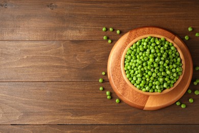 Fresh green peas in bowl on wooden table, top view. Space for text