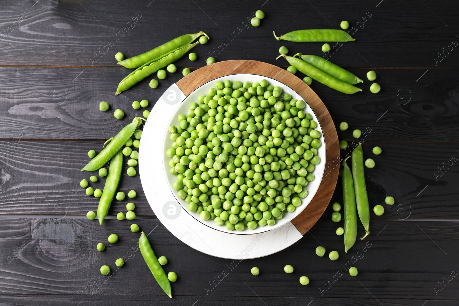 Photo of Fresh green peas in bowl and pods on black wooden table, flat lay