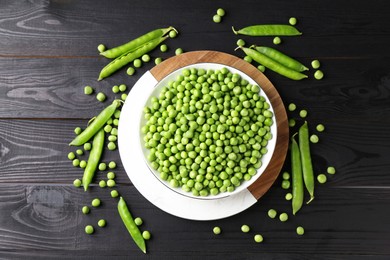 Photo of Fresh green peas in bowl and pods on black wooden table, flat lay