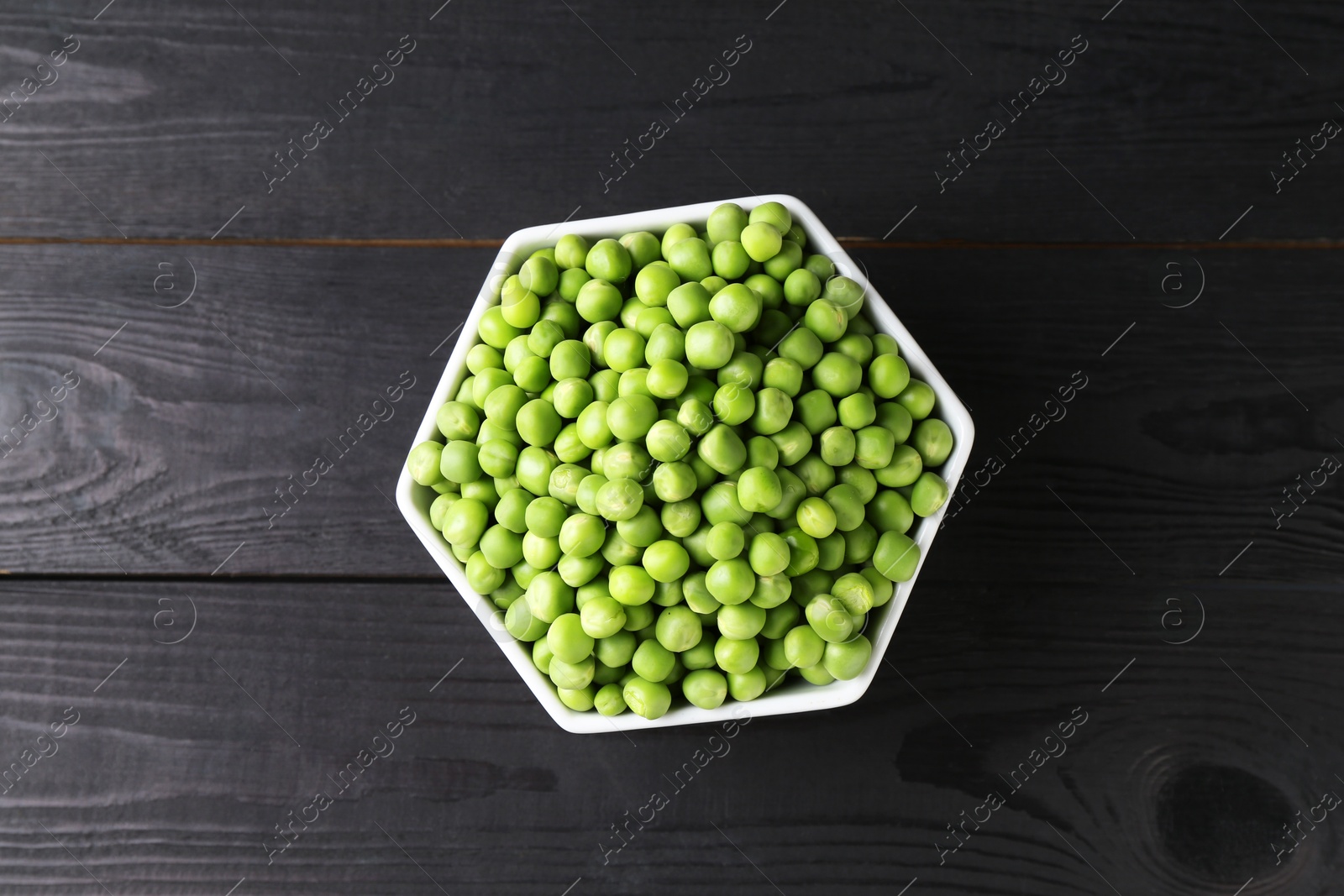 Photo of Fresh green peas in bowl on black wooden table, top view