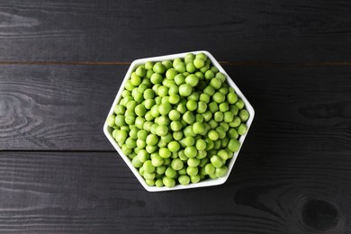 Fresh green peas in bowl on black wooden table, top view