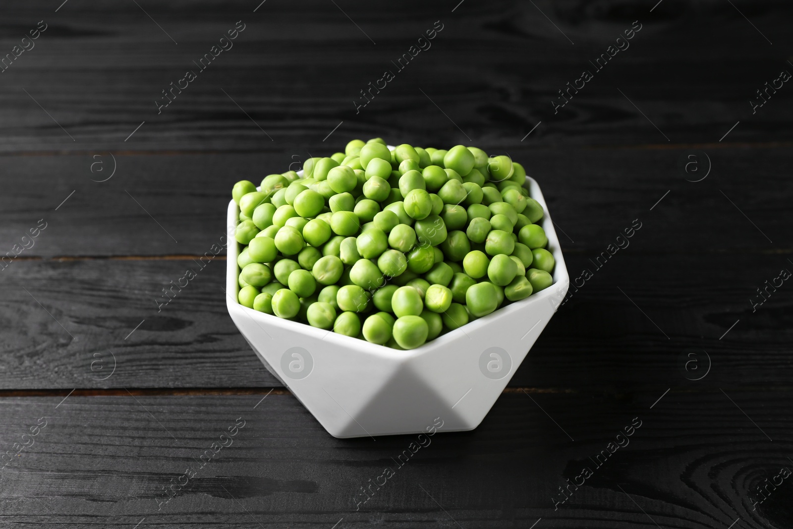 Photo of Fresh green peas in bowl on black wooden table