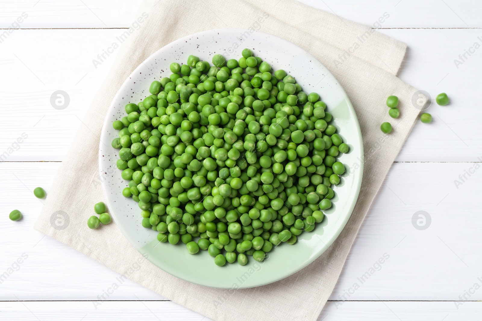 Photo of Fresh green peas in plate on white wooden table, top view