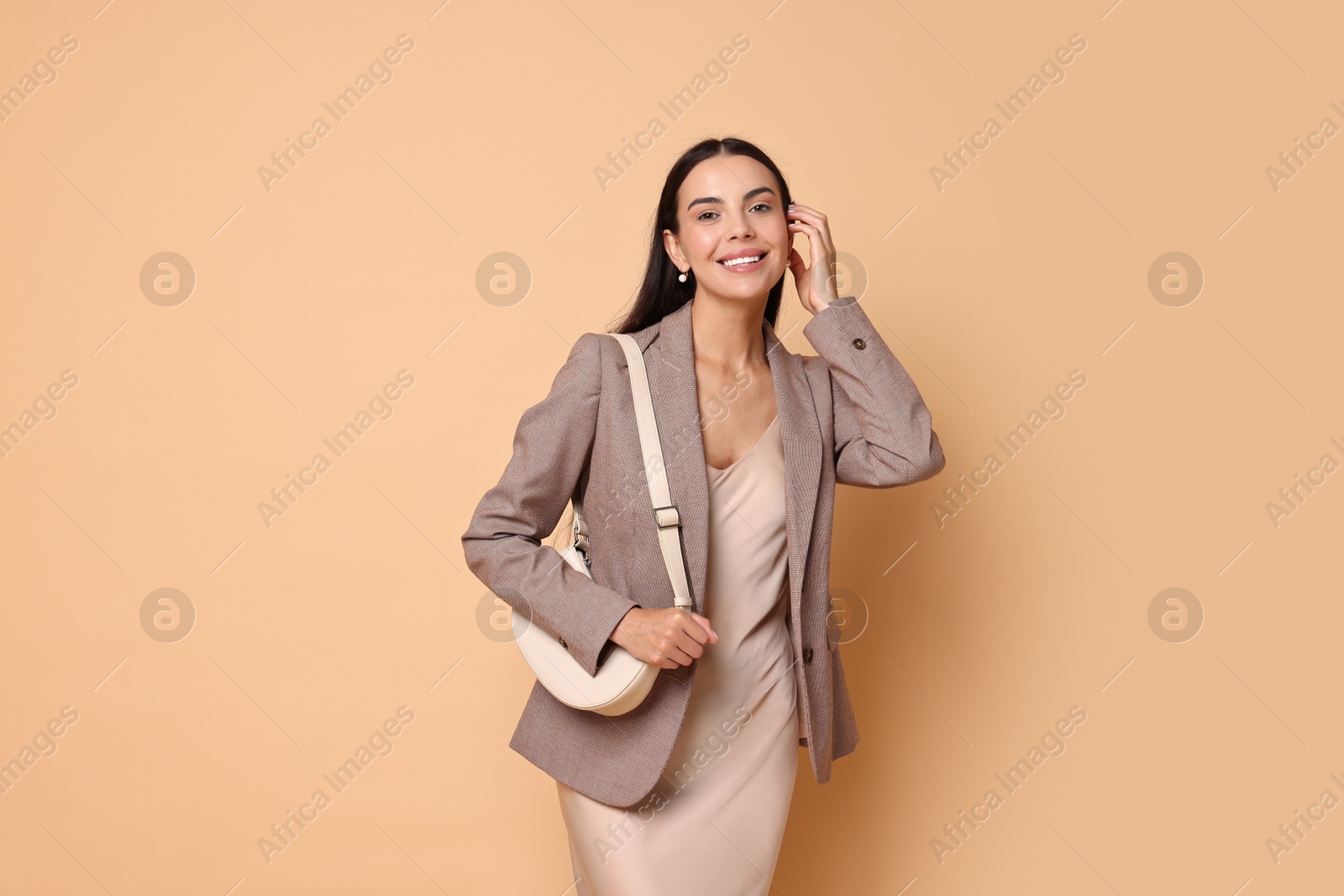 Photo of Beautiful woman in stylish jacket with bag on pale orange background