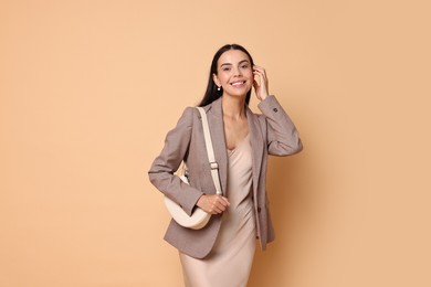 Photo of Beautiful woman in stylish jacket with bag on pale orange background