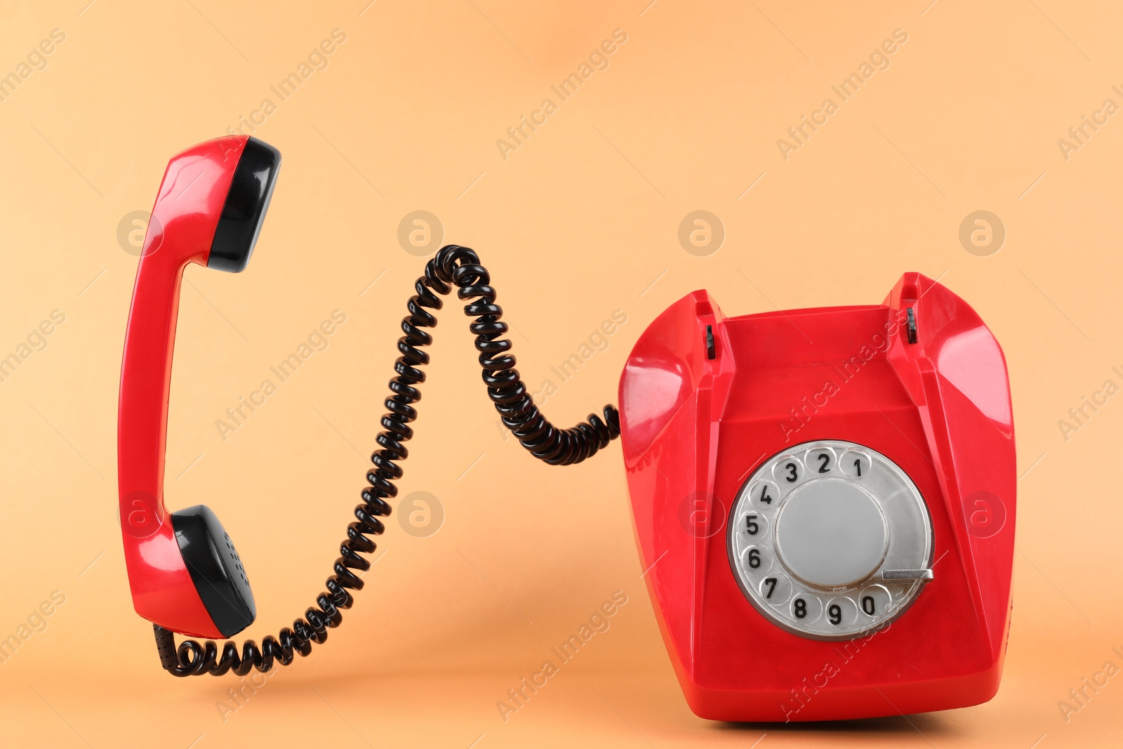 Photo of One red telephone with handset on pale orange background