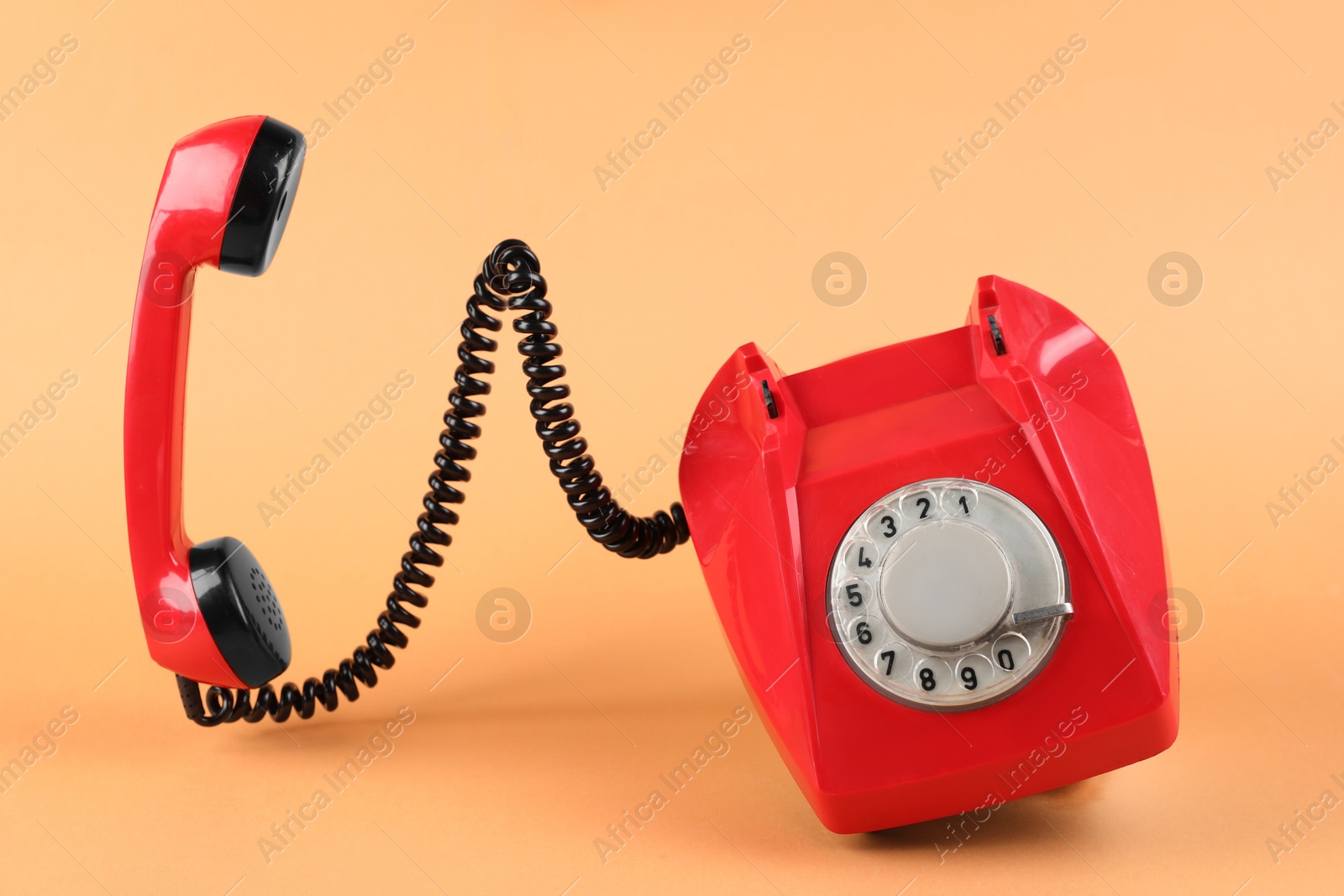 Photo of One red telephone with handset on pale orange background