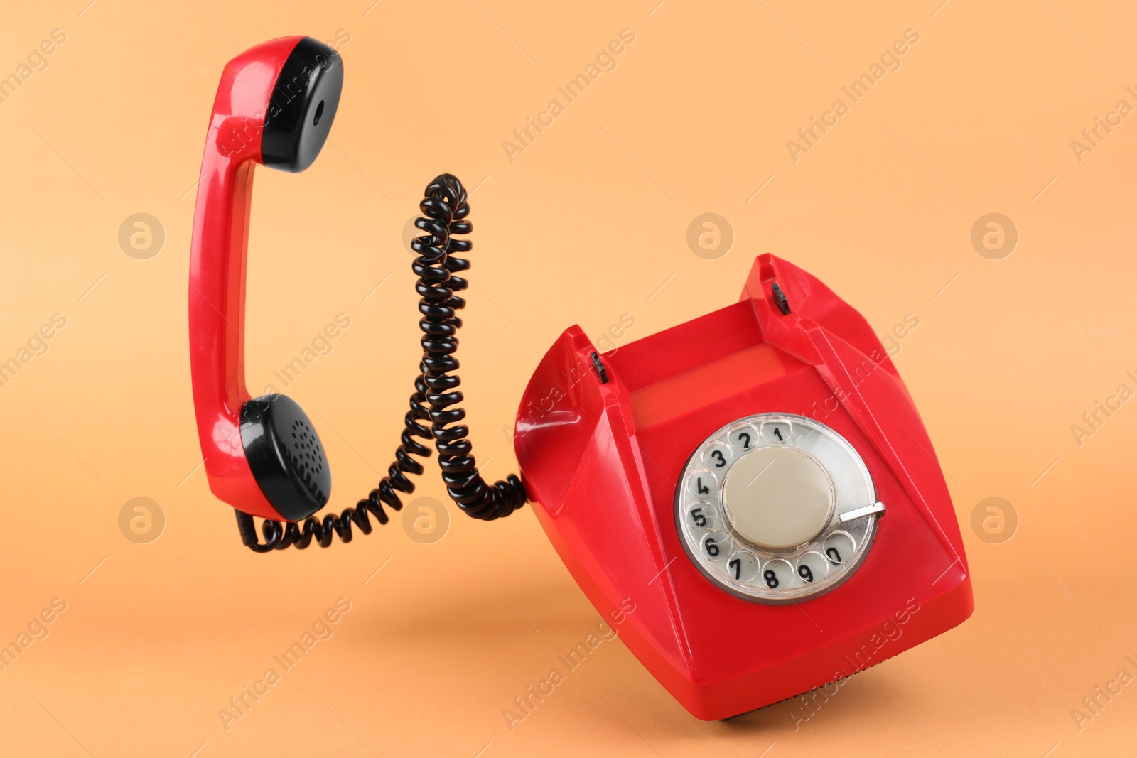 Photo of One red telephone with handset on pale orange background