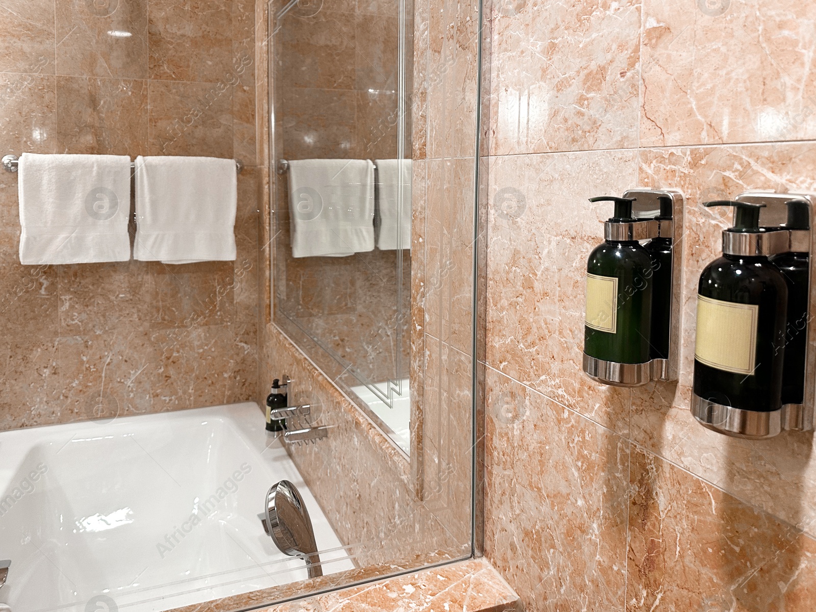 Photo of Bottles with body care products on tiled wall in hotel bathroom