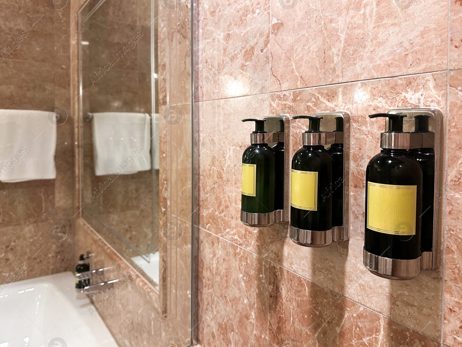 Photo of Bottles with body care products on tiled wall in hotel bathroom