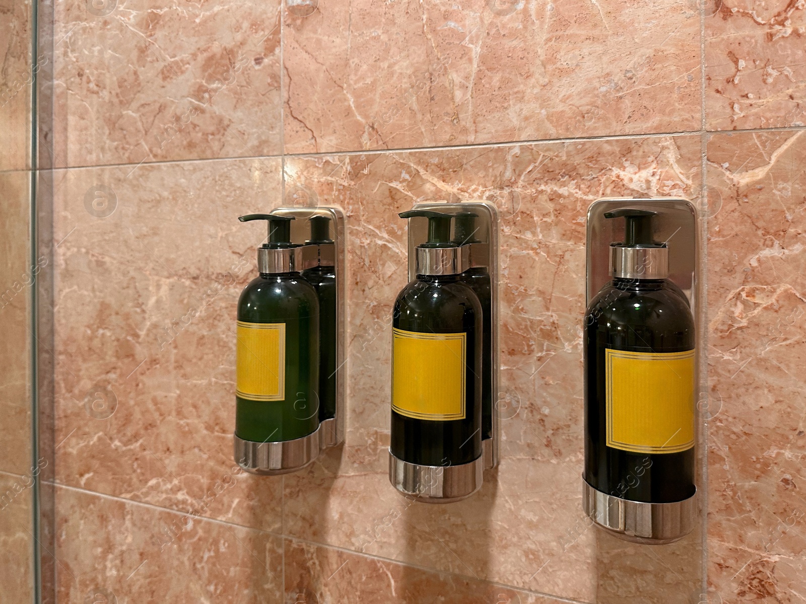 Photo of Bottles with body care products on tiled wall in hotel bathroom