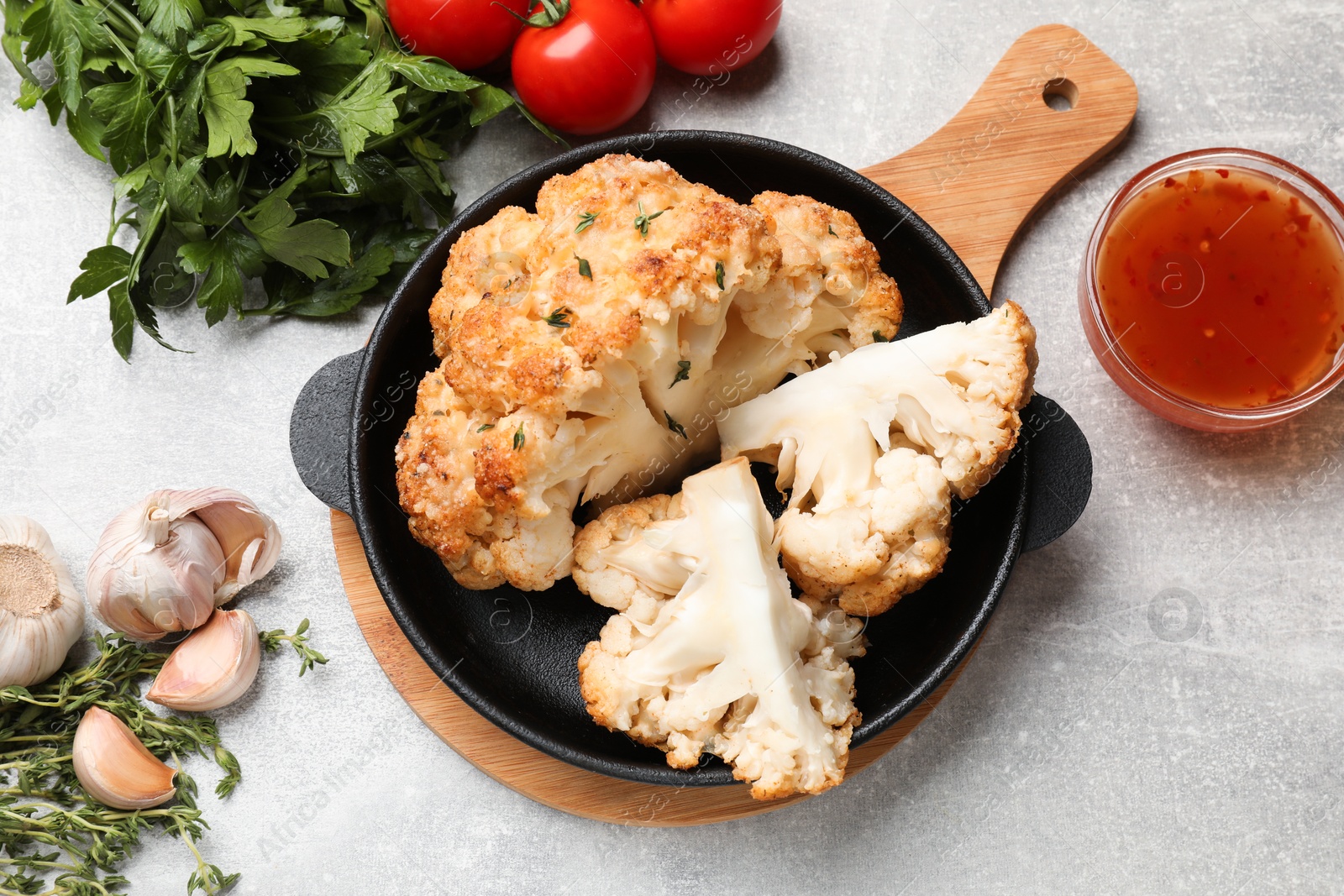 Photo of Delicious baked cauliflower in baking dish and products on gray textured table, flat lay