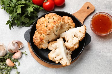 Delicious baked cauliflower in baking dish and products on gray textured table, flat lay