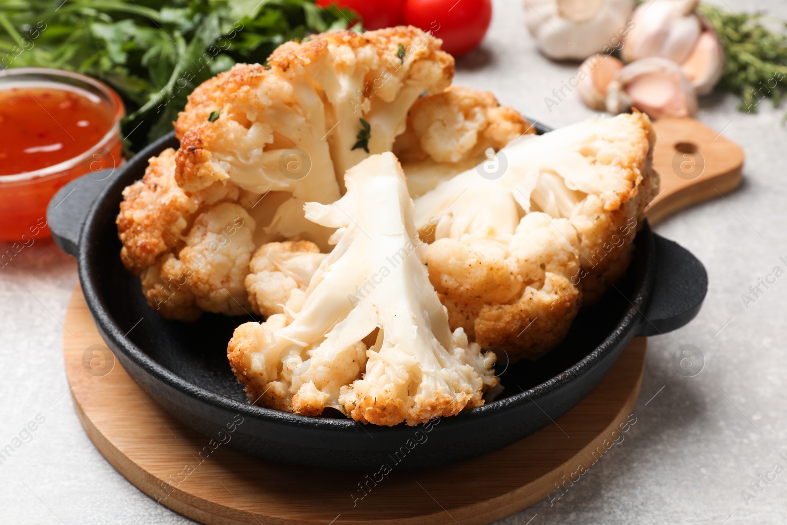 Photo of Delicious baked cauliflower in baking dish and products on gray textured table, closeup