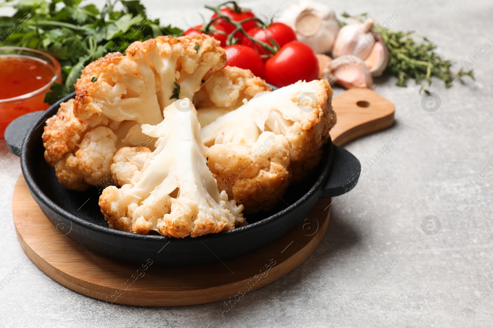 Photo of Delicious baked cauliflower in baking dish and products on gray textured table, closeup