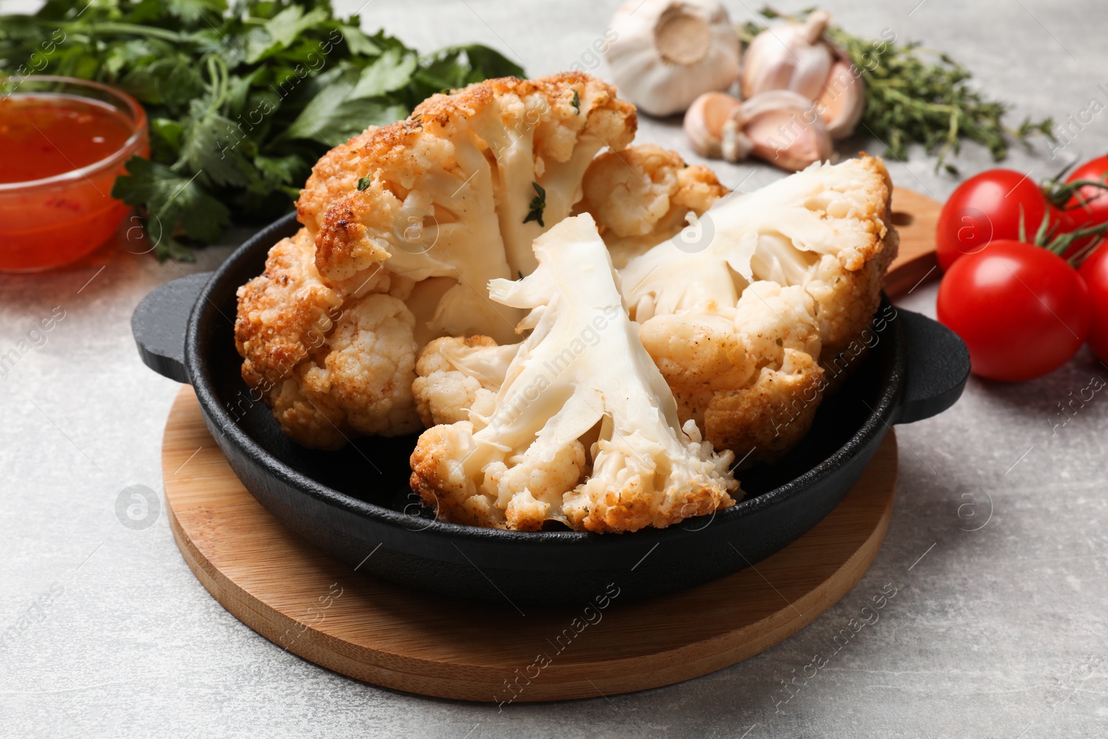 Photo of Delicious baked cauliflower in baking dish and products on gray textured table, closeup