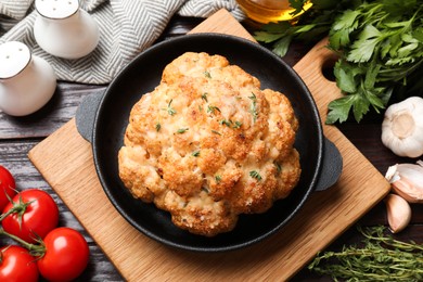 Photo of Delicious baked cauliflower in baking dish and products on wooden table, flat lay