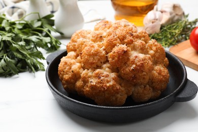 Delicious baked cauliflower in baking dish and products on white table, closeup