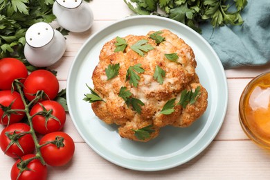 Photo of Delicious baked cauliflower, tomatoes, oil and spices on wooden table, flat lay