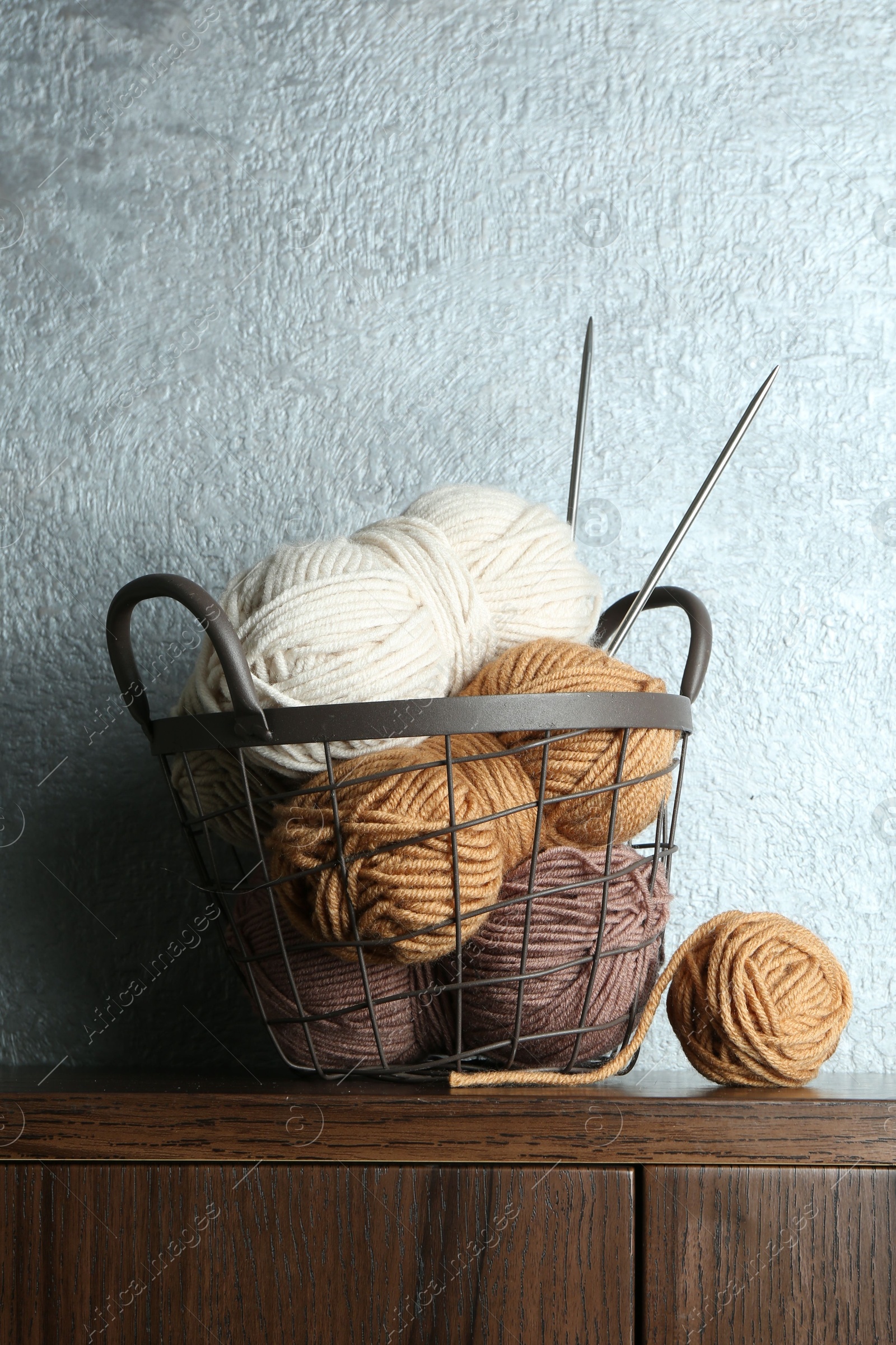 Photo of Basket with colorful yarns and knitting needles on wooden shelf indoors