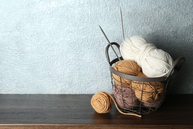 Photo of Basket with colorful yarns and knitting needles on wooden shelf indoors. Space for text