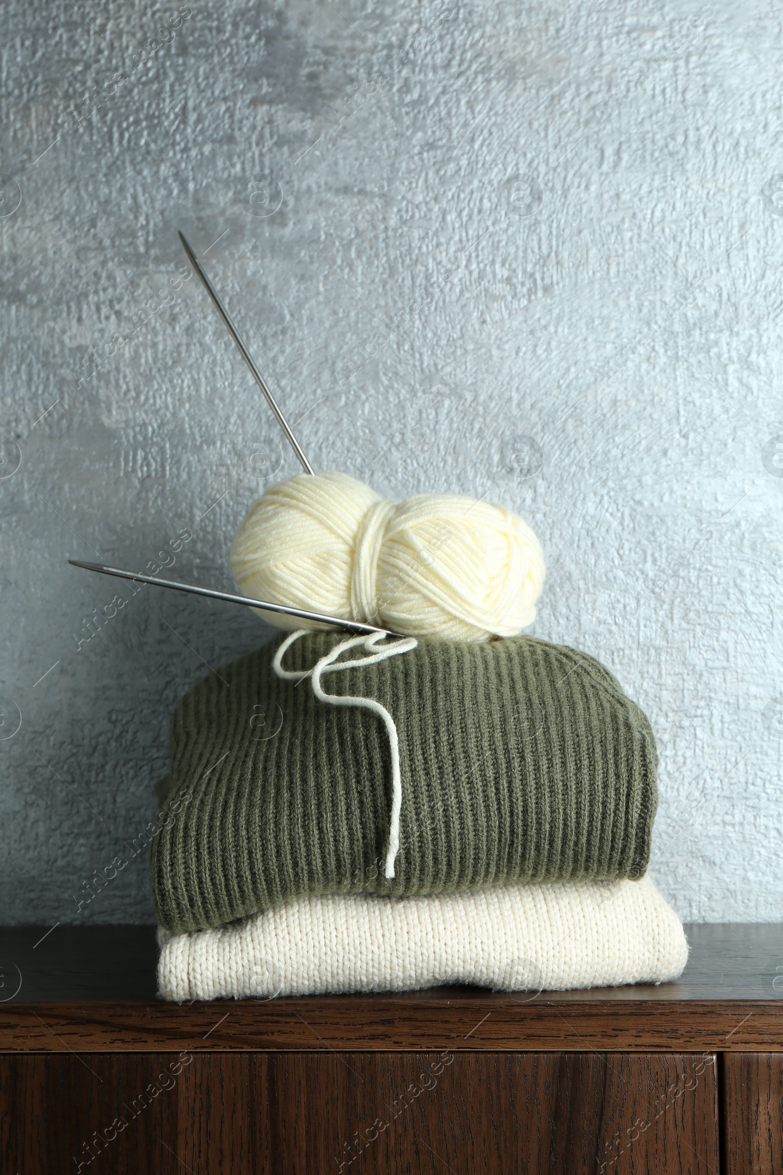 Photo of Skein of yarn, knitting needles and sweaters on wooden shelf indoors