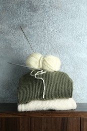 Skein of yarn, knitting needles and sweaters on wooden shelf indoors