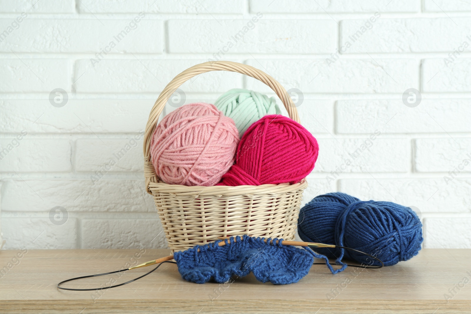 Photo of Bright yarns, knitting needles and pattern sample on wooden shelf indoors