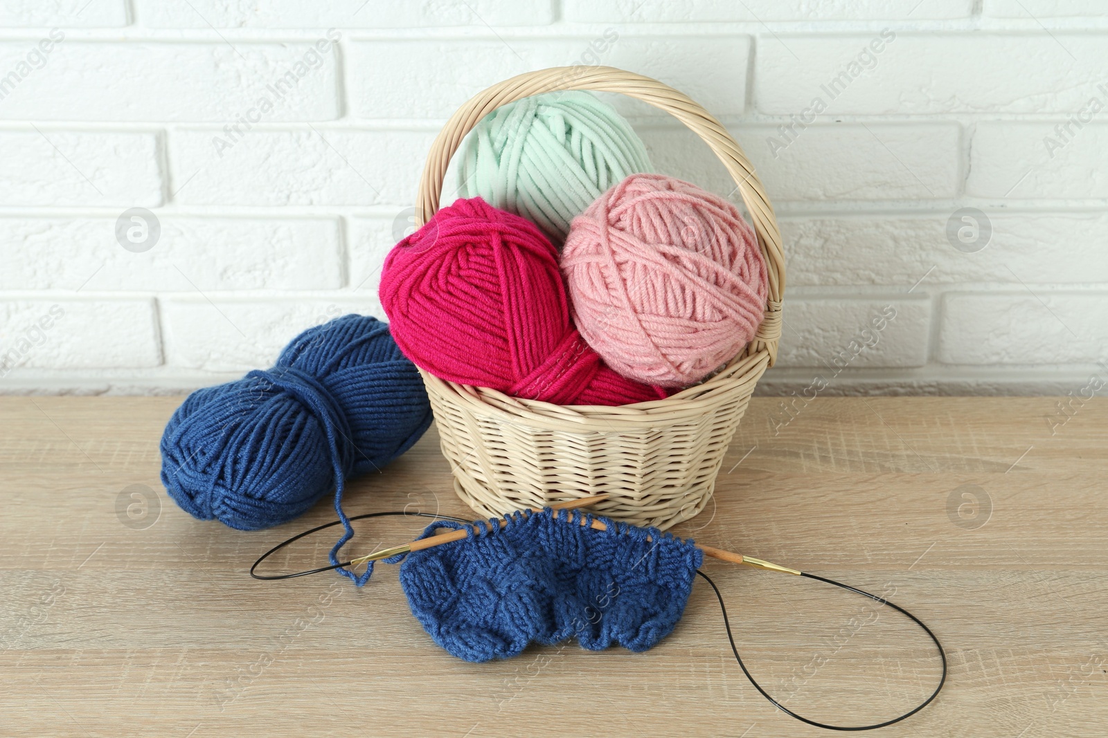 Photo of Bright yarns, knitting needles and pattern sample on wooden shelf indoors