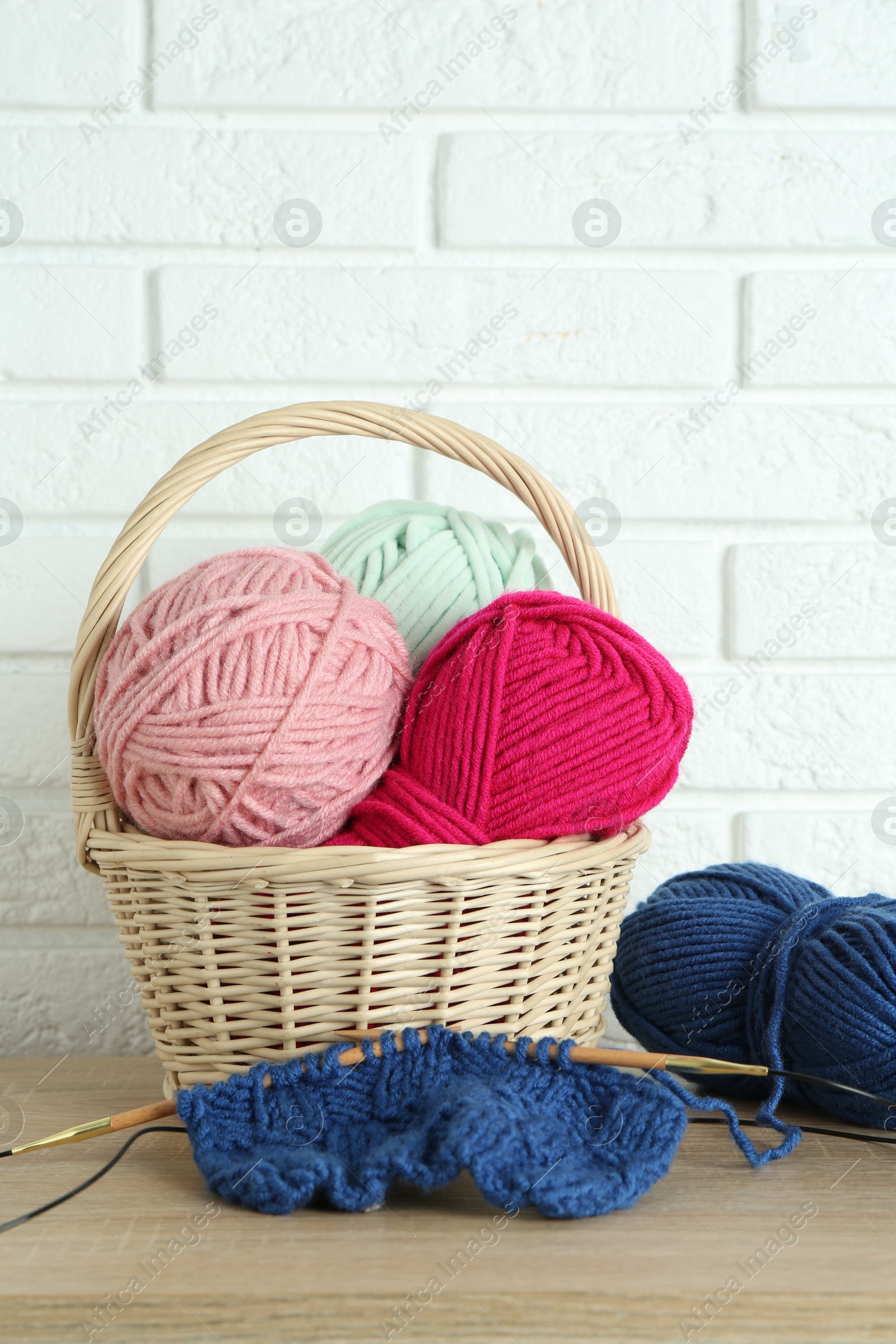 Photo of Bright yarns, knitting needles and pattern sample on wooden shelf indoors