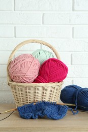 Bright yarns, knitting needles and pattern sample on wooden shelf indoors