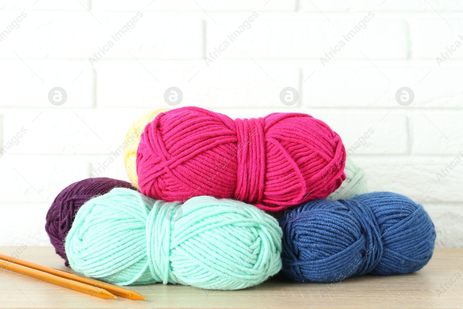 Photo of Skeins of yarn and knitting needles on wooden shelf near white brick wall