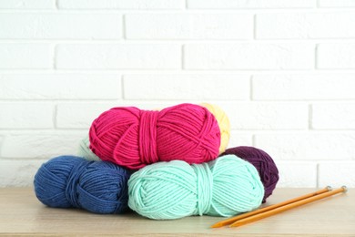 Photo of Skeins of yarn and knitting needles on wooden shelf near white brick wall