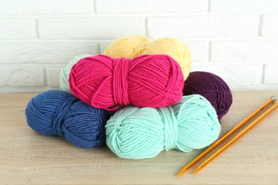 Photo of Skeins of yarn and knitting needles on wooden shelf near white brick wall