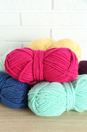 Photo of Skeins of yarn on wooden shelf near white brick wall