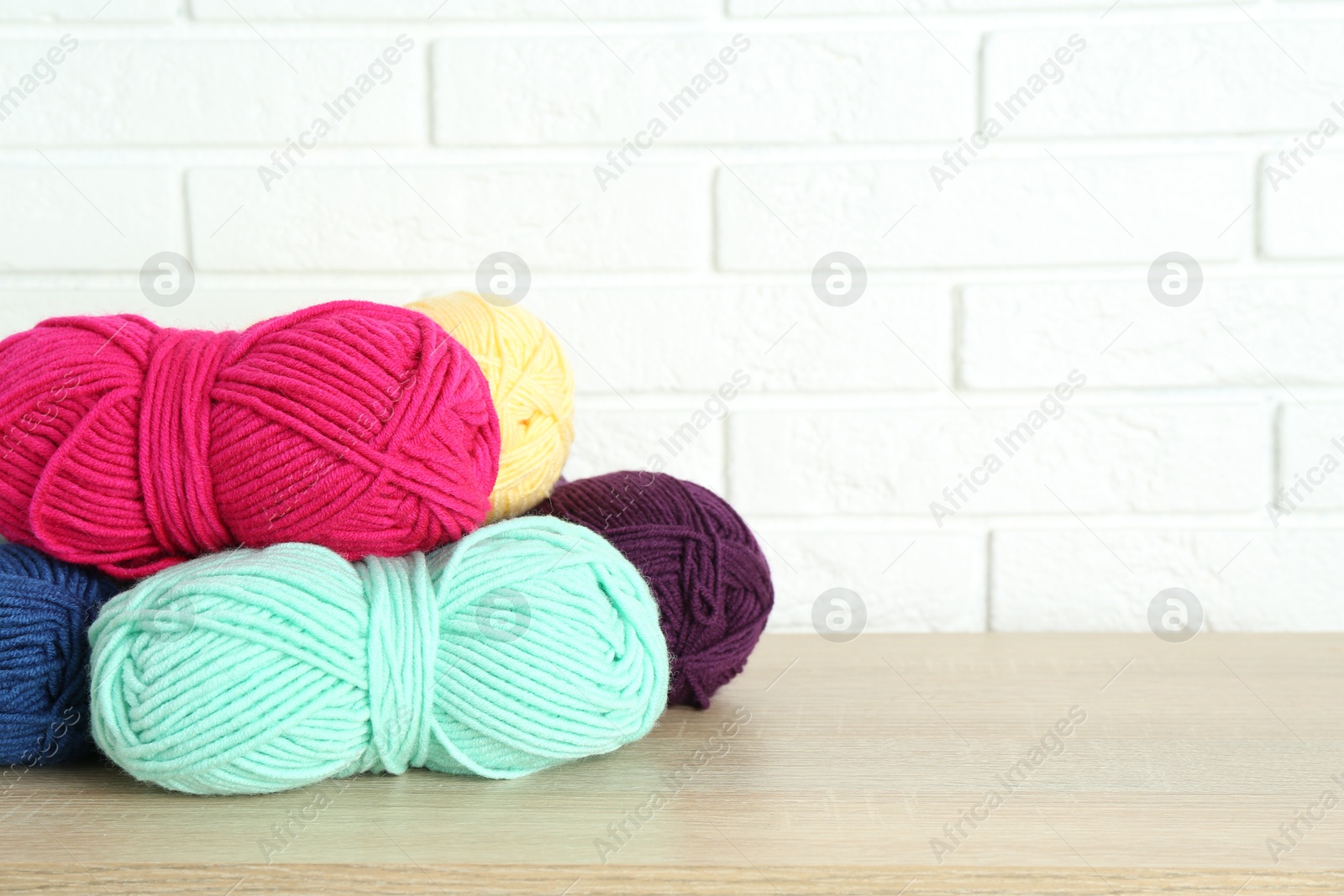 Photo of Skeins of yarn on wooden shelf near white brick wall. Space for text